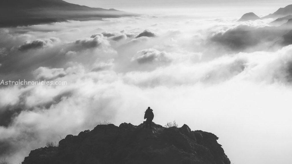 person standing at the edge of a mountain facing clouds during day