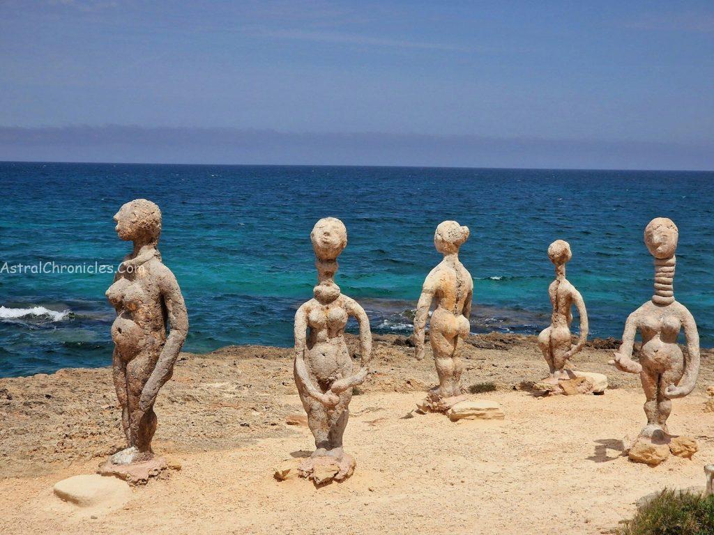 Stone figures stand on a rocky shore by the sea